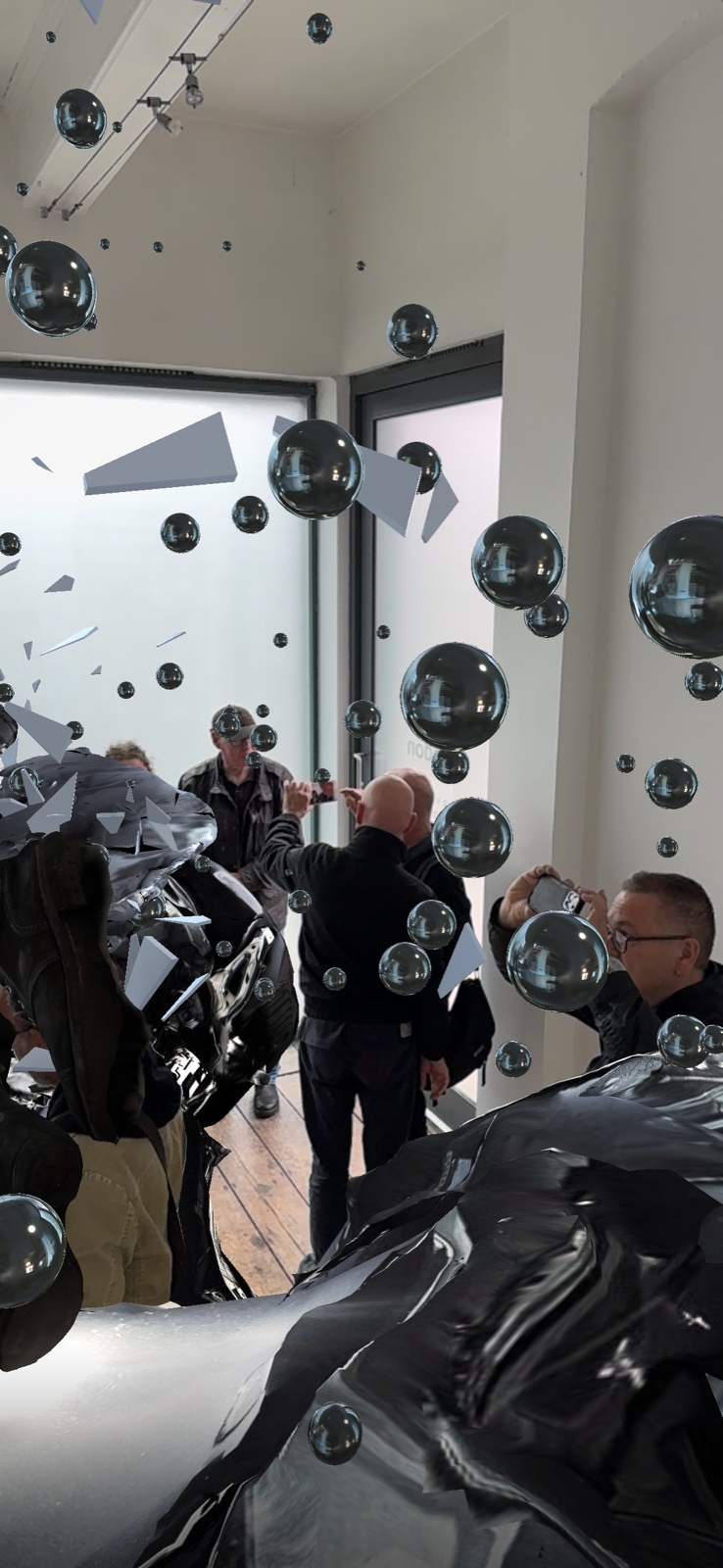 A visitor holding up a phone beneath the augmented-reality crash suspended above the gallery floor.