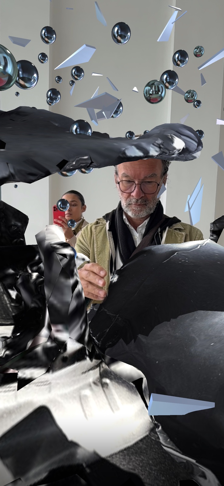 The two figures caught in an embrace amid mirrored spheres, seen through a phone at MOCA London.
